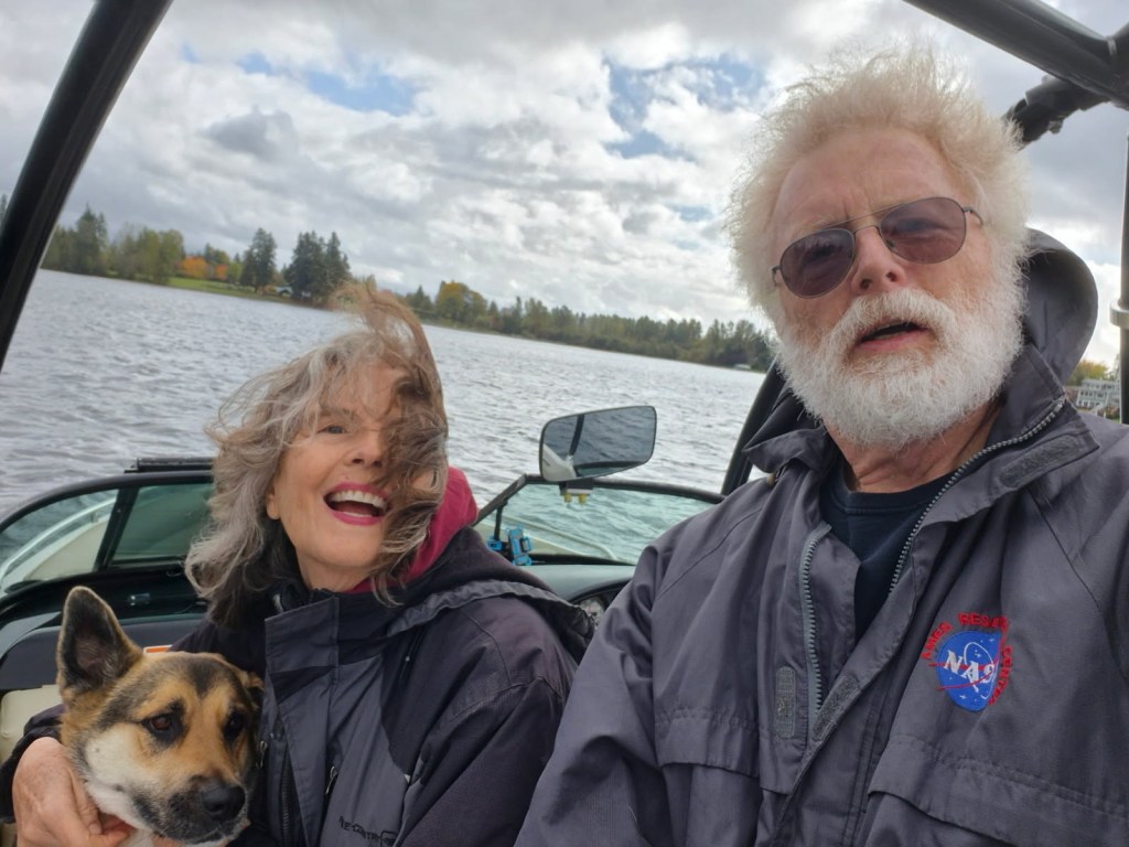 A German shepherd, a woman, and a man in a boat on a lake on a windy day
