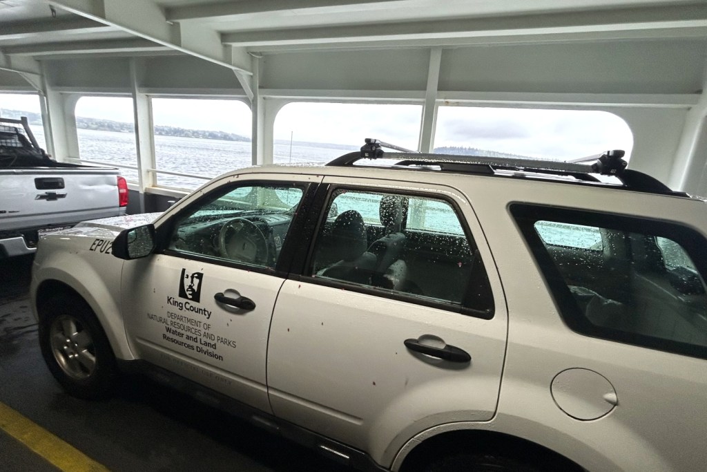 A white SUV with a King County logo on the lower deck of a Washington State ferry