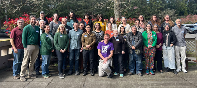 A large group of people stand together, smiling for the camera.